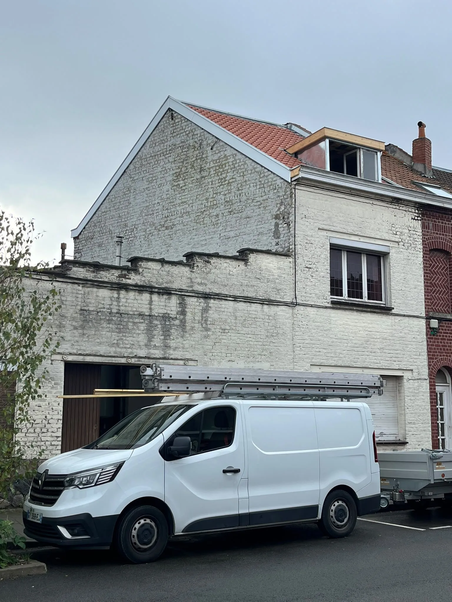 Façade blanche en briques, toiture neuve à tuiles rouges avec lucarne en zinc, camionnette et échelle devant