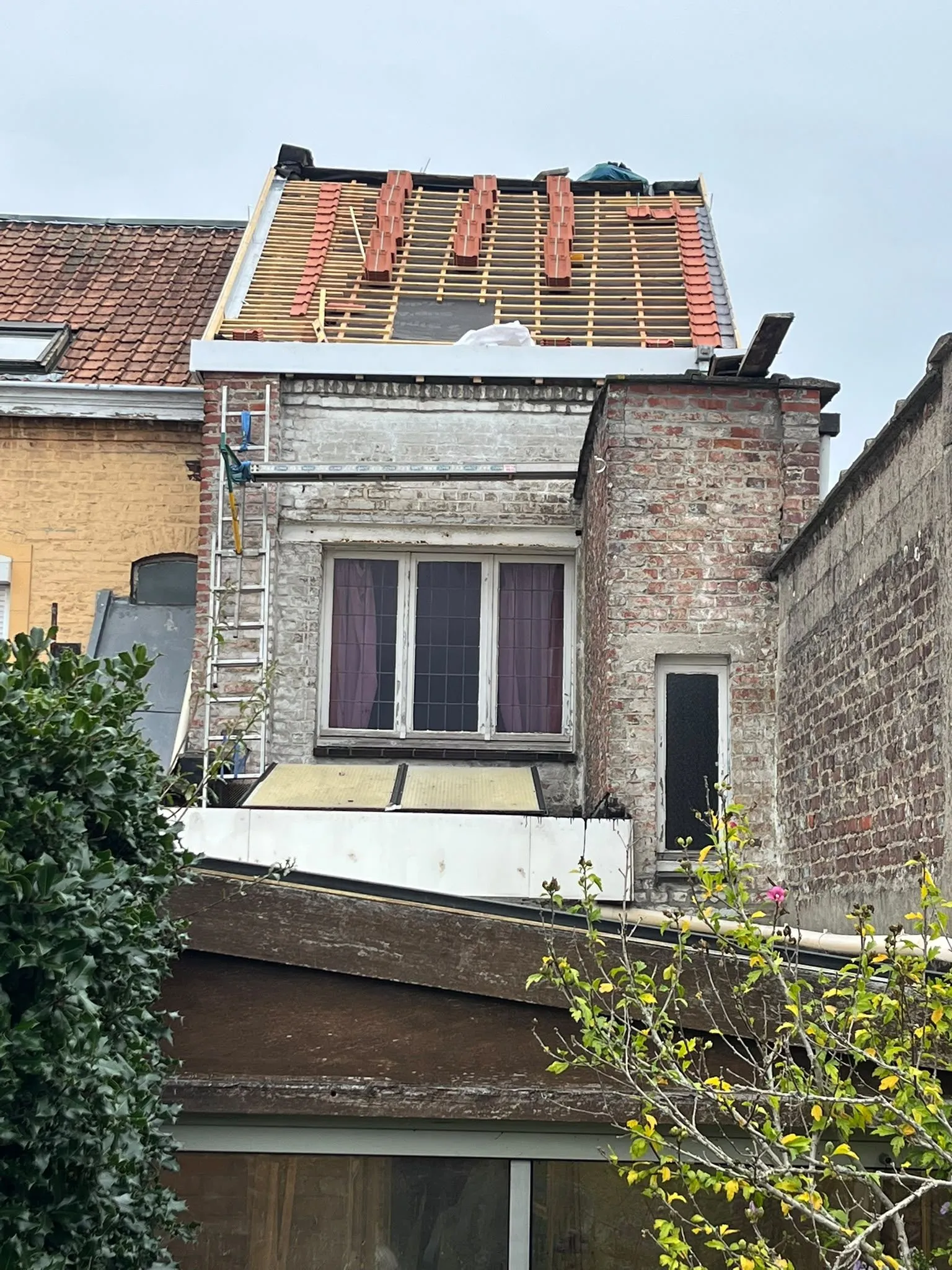 Charpente de toit à Tourcoing avec lattes en bois, quelques tuiles posées et échelle contre la façade en briques