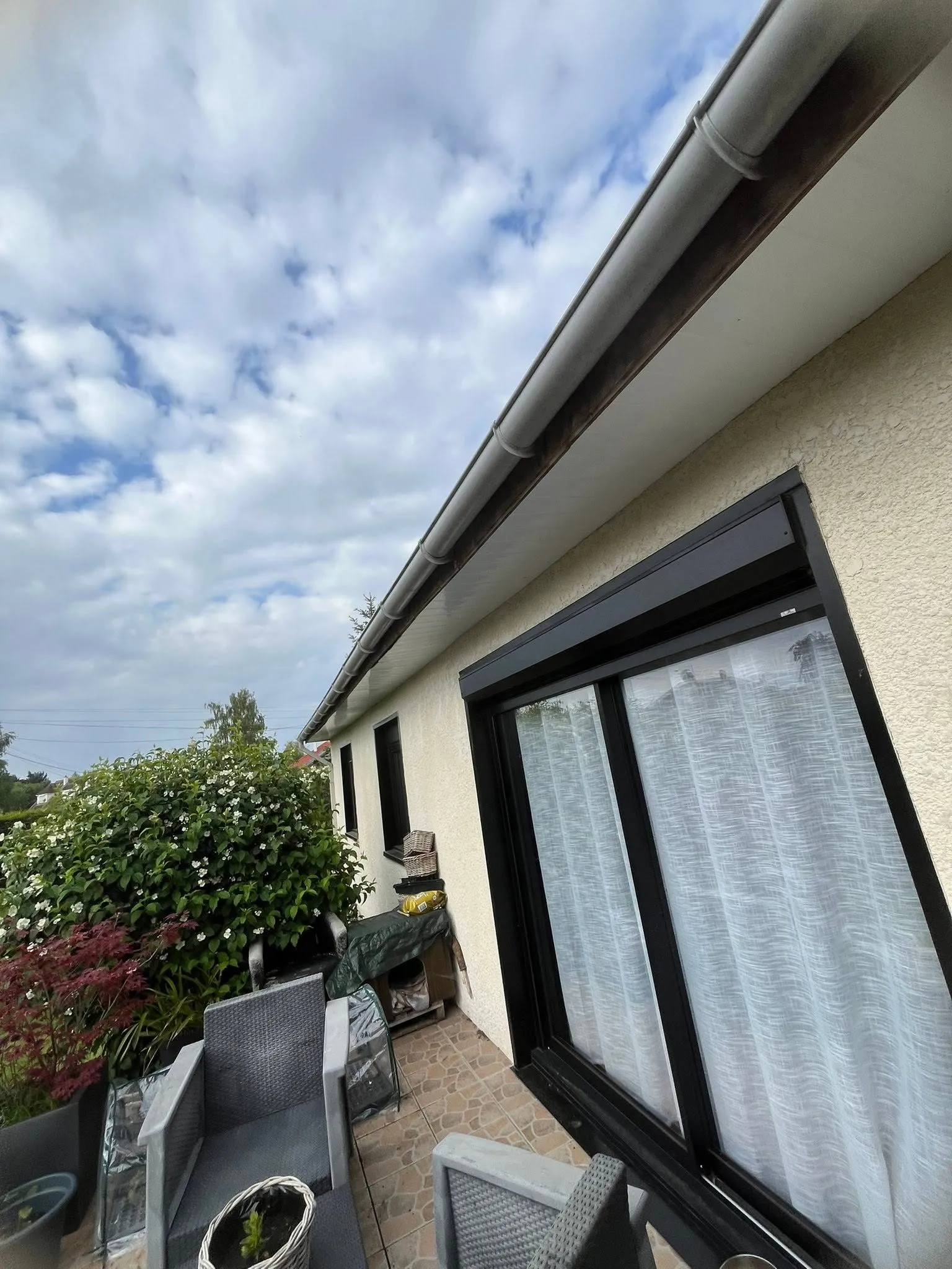 Gouttière en zinc et sous-face au-dessus d'une baie vitrée noire, côté terrasse, à Raimbeaucourt