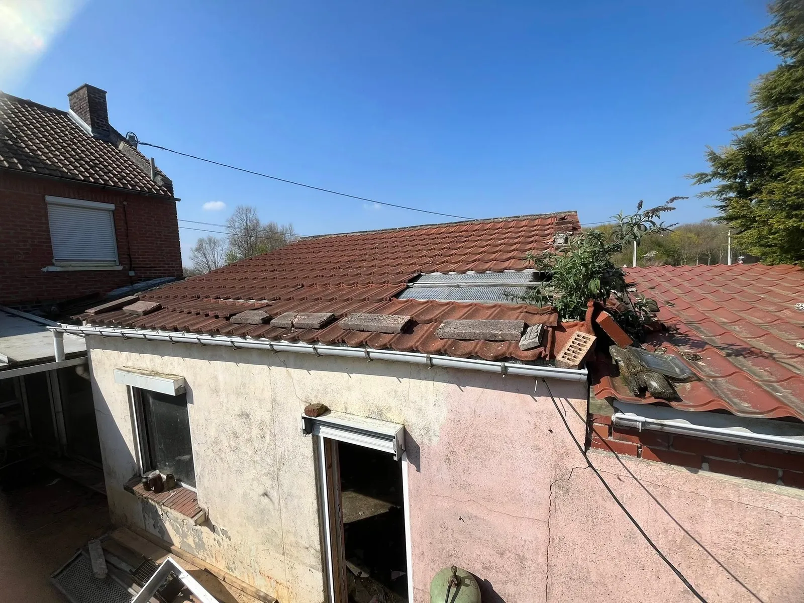 Ancienne toiture en tuiles de terre cuite abîmée, avec tuiles déplacées et plante, avant travaux à Ostricourt