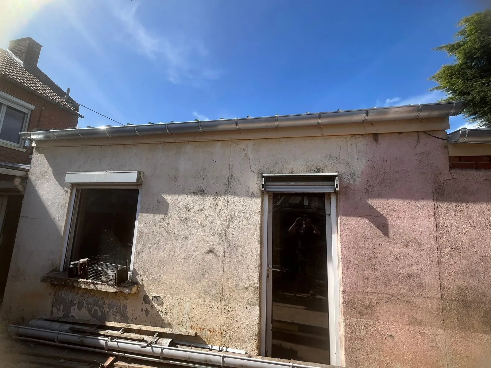 Façade de la dépendance en enduit rose, surmontée d'une gouttière ronde en zinc, avant la pose du bac acier