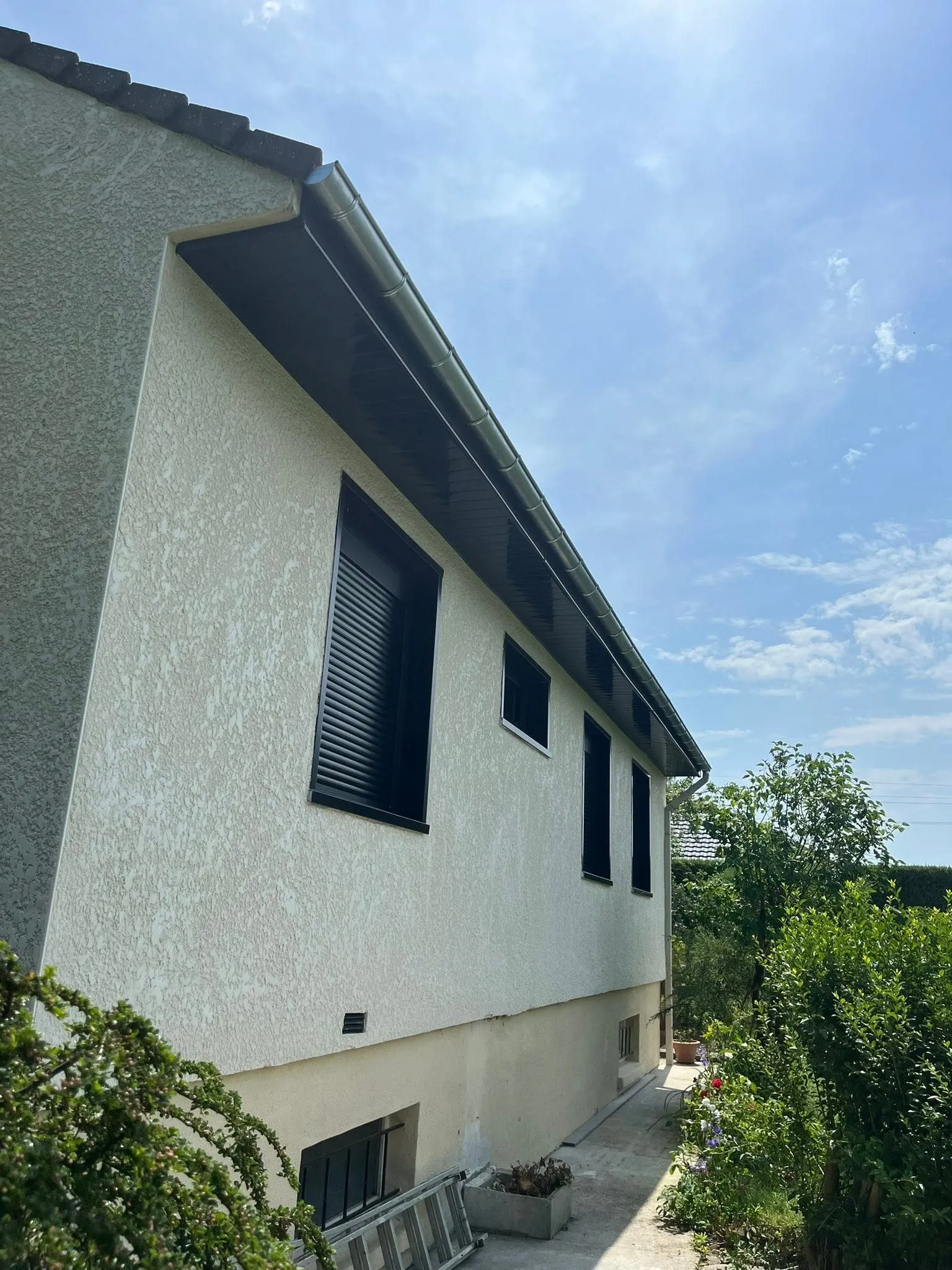 Façade crépie d'une maison à Raimbeaucourt, sous-face noire et gouttière en zinc neuve sous le toit
