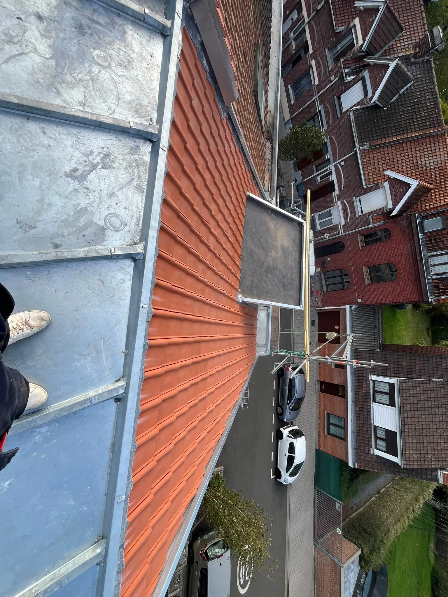 Vue plongeante sur un pan de tuiles rouges et une plateforme en zinc, avec une rue et des voitures en contrebas