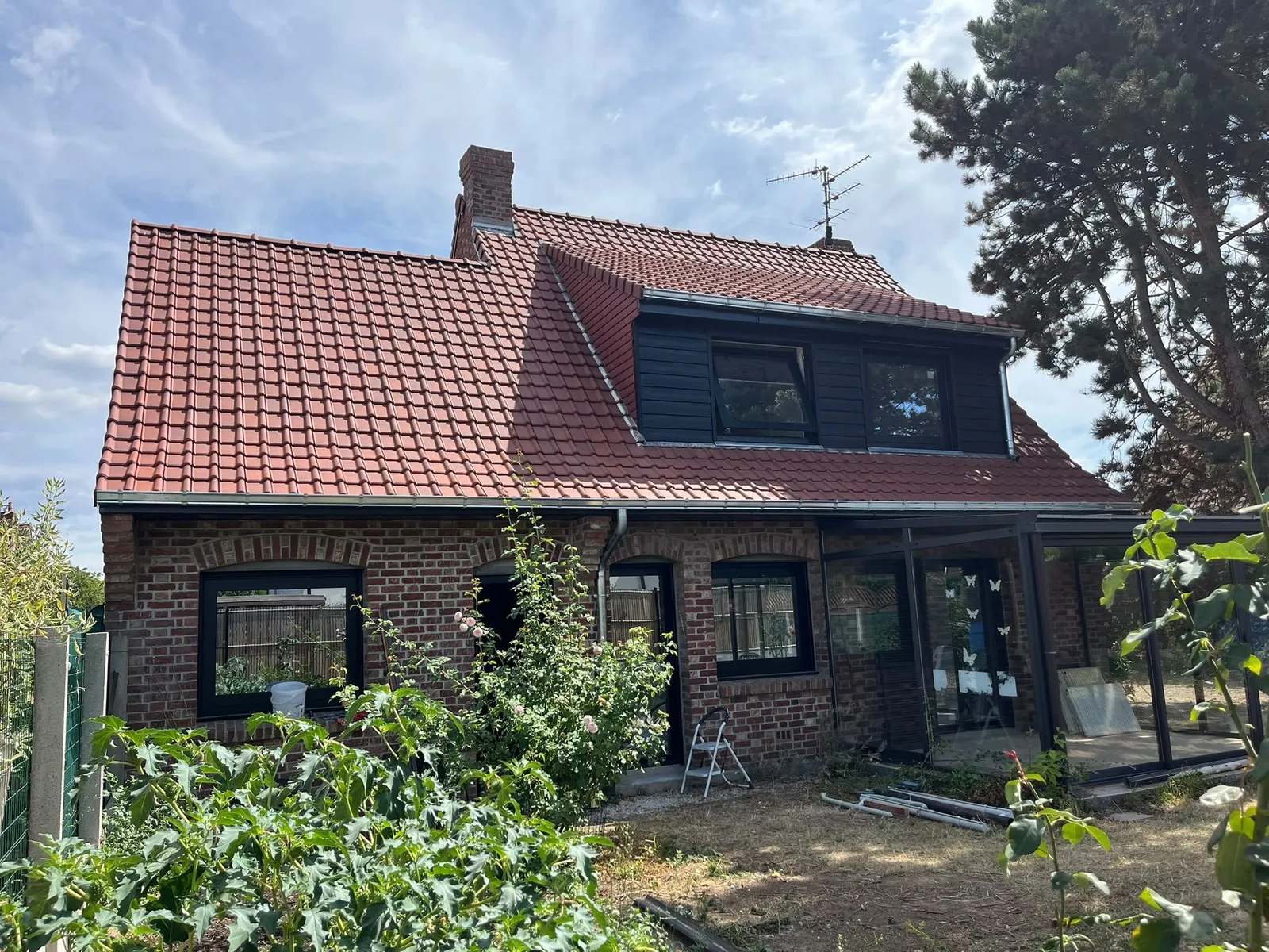 Arrière de la maison en brique : toiture en tuiles rouges, lucarne à bardage noir et gouttière en zinc