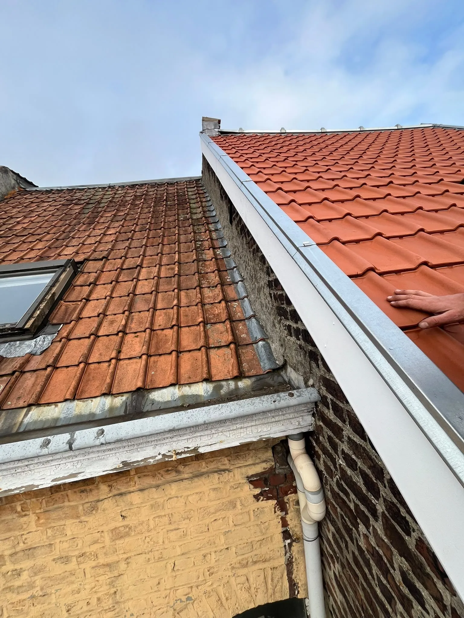 Toiture neuve en tuiles rouges avec chéneau en zinc, à côté d'un ancien toit à fenêtre de toit