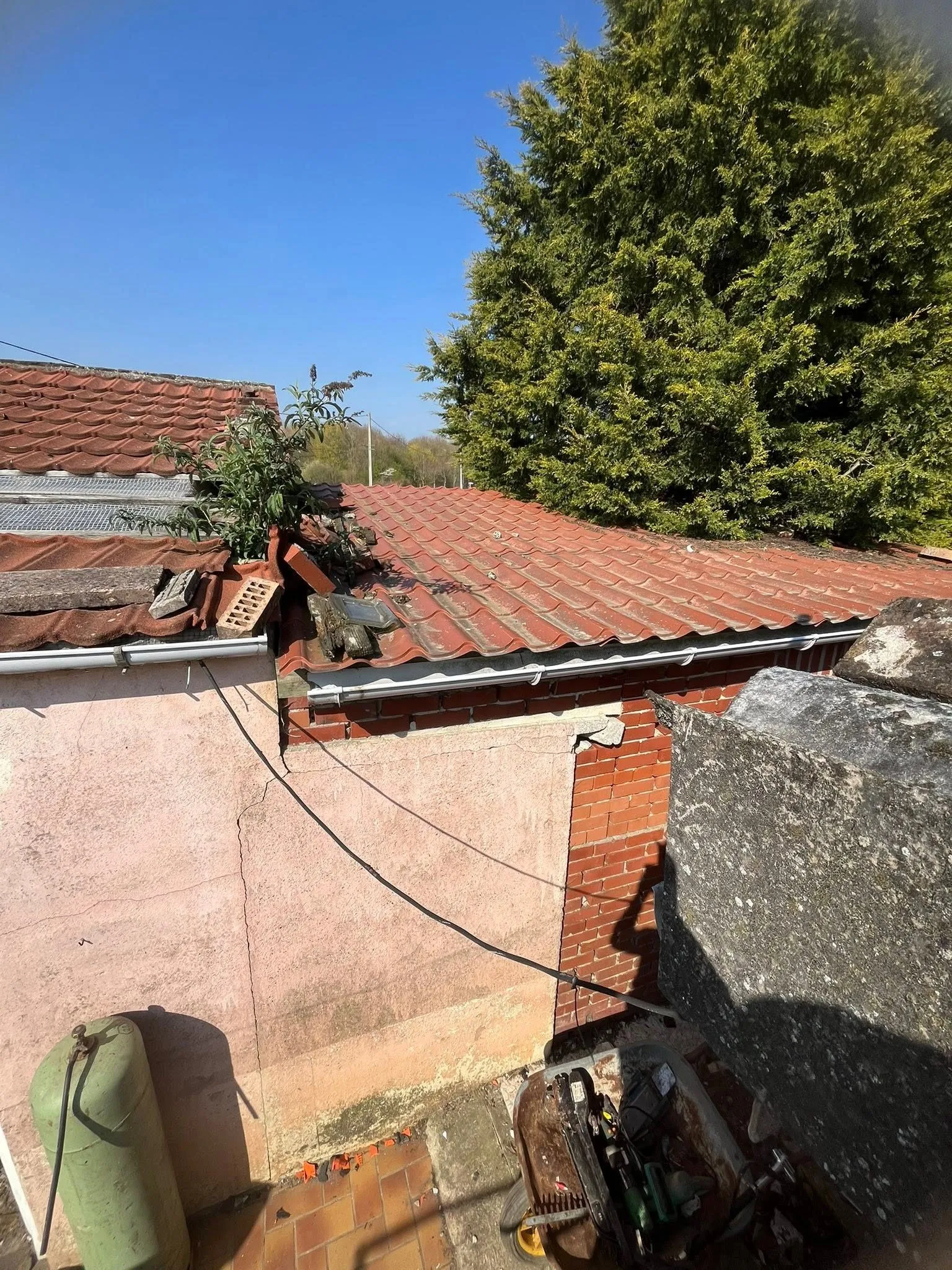 Toit de tuiles en terre cuite avec briques et débris posés dessus, gouttière en zinc en bas de pente